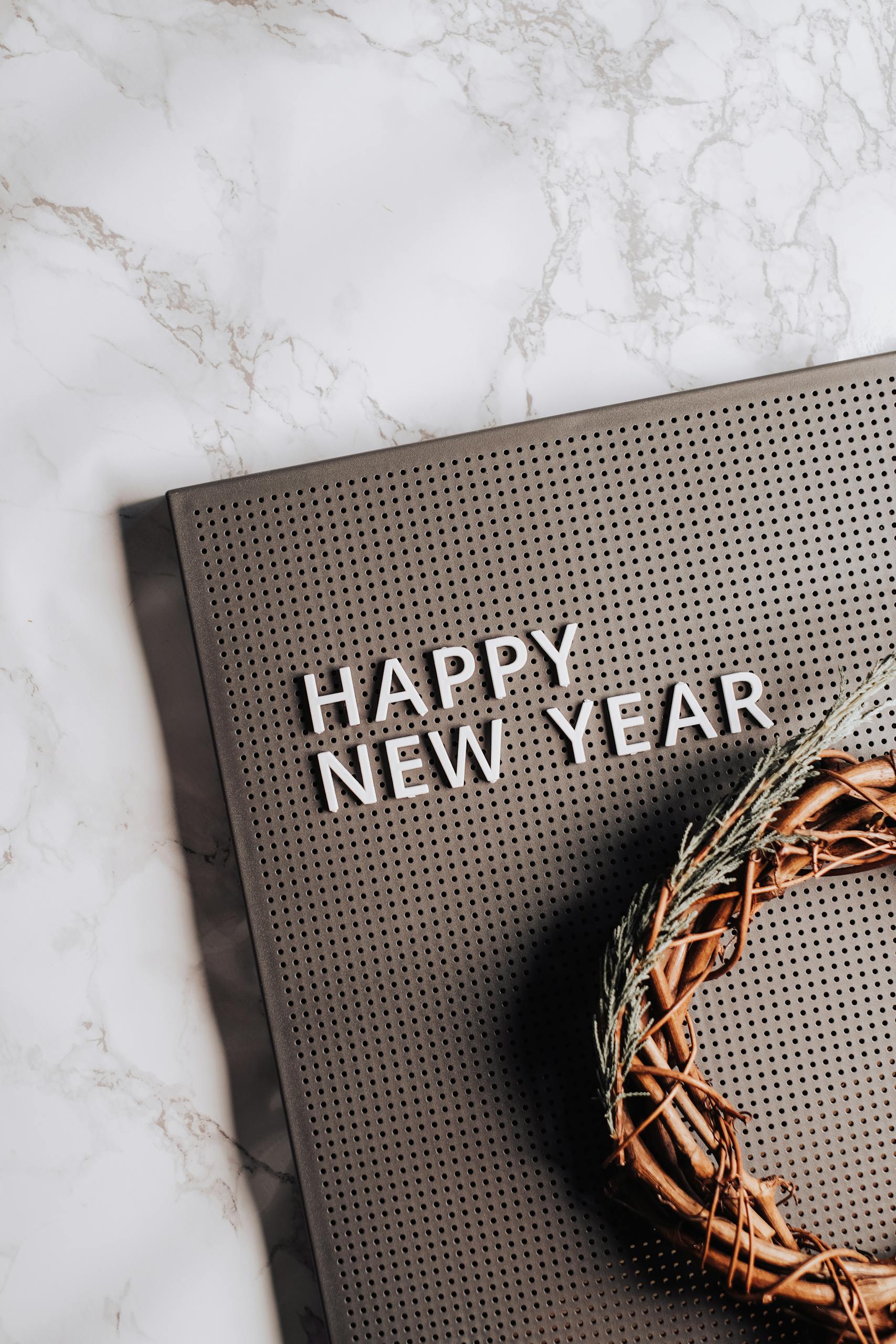 Wooden wreath and pegboard displaying 'Happy New Year' on marble surface.